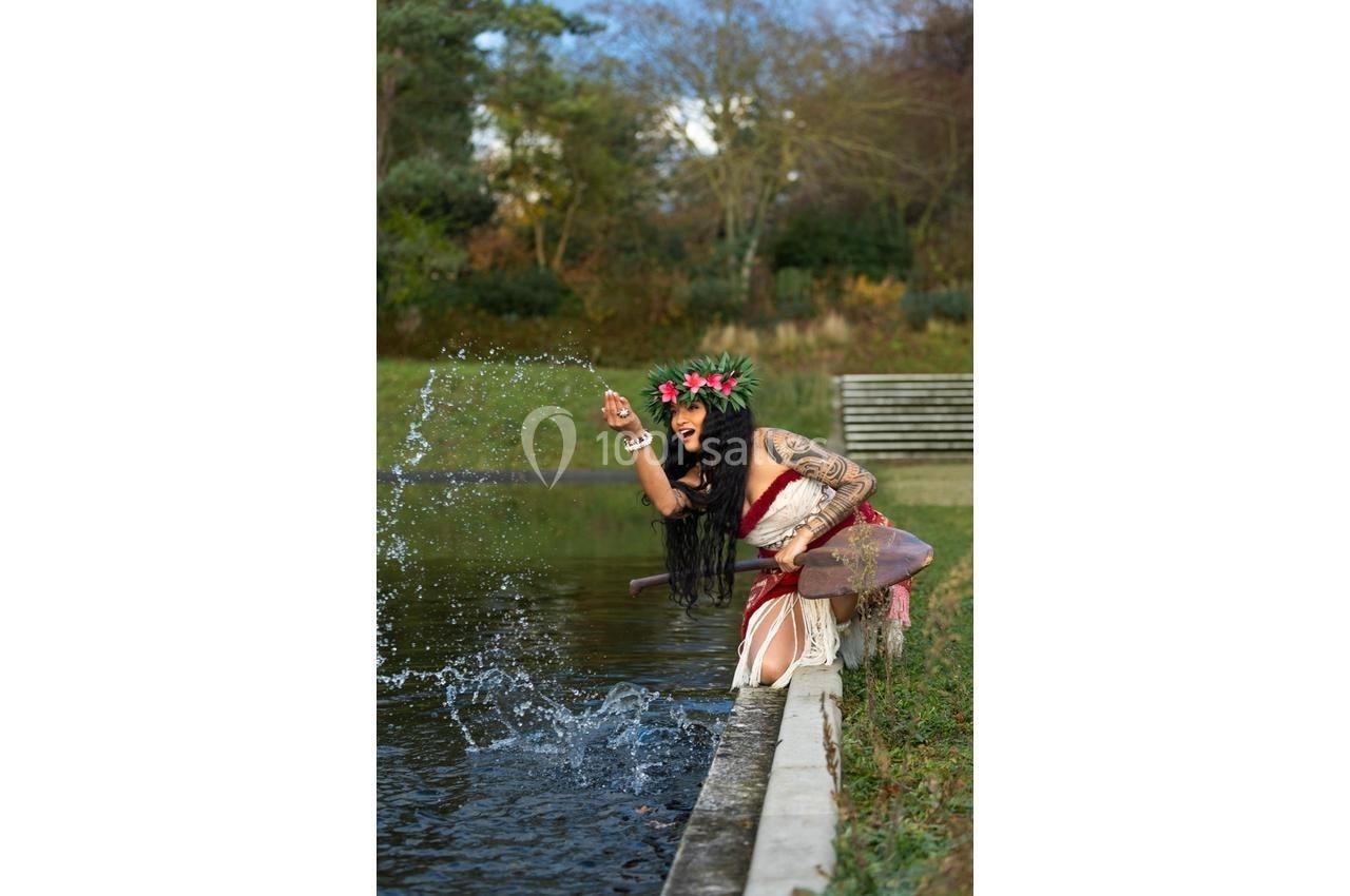 Une femme en tenue traditionnelle, couronnée de fleurs, éclabousse l'eau d'un bassin en extérieur.