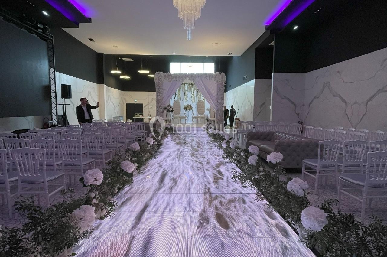 Allée décorée de fleurs blanches menant à une arche nuptiale dans une salle de réception élégante et moderne.