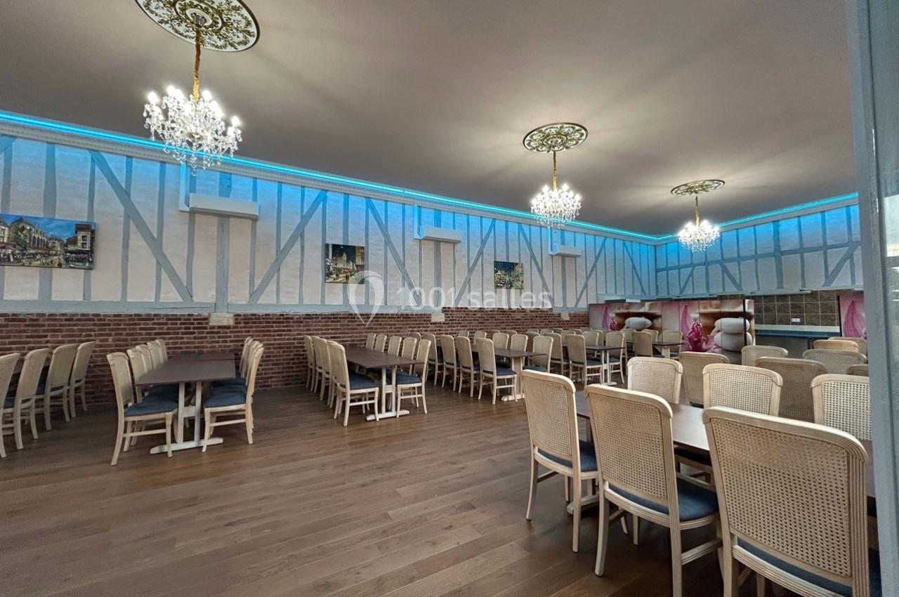 Salle de réception spacieuse avec parquet, tables en bois, chaises en osier et lustres suspendus.