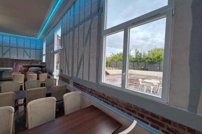 Salle lumineuse avec des tables en bois, des chaises en osier et de grandes fenêtres donnant sur une terrasse extérieure.