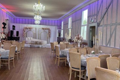 Salle lumineuse avec des tables en bois, des chaises en osier et de grandes fenêtres donnant sur une terrasse extérieure.