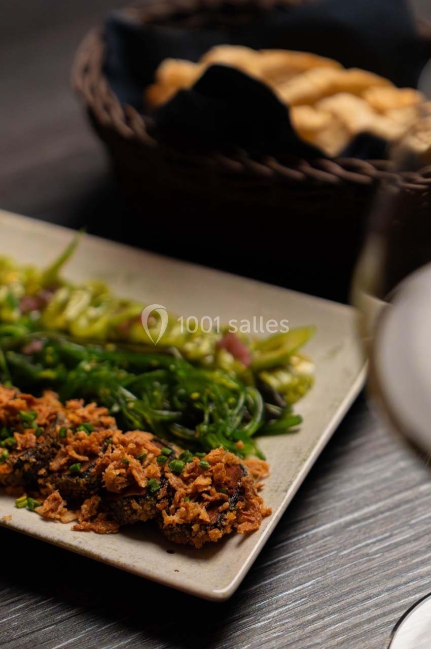 Assiette contenant des légumes verts et des morceaux de viande panés, avec un panier de pain en arrière-plan.