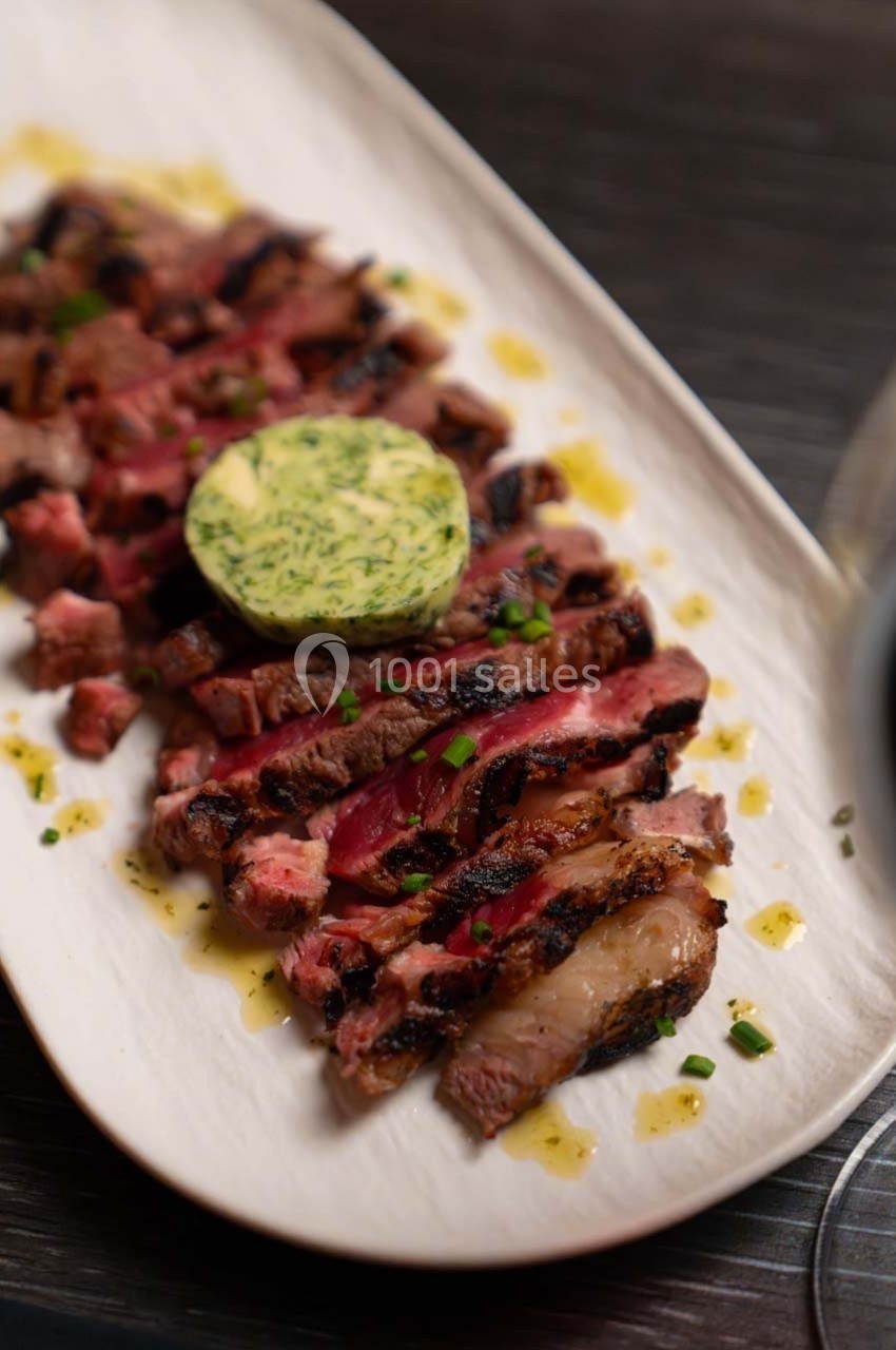 Tranches de steak grillé garnies de beurre aux herbes, servies sur une assiette blanche avec une sauce légère.