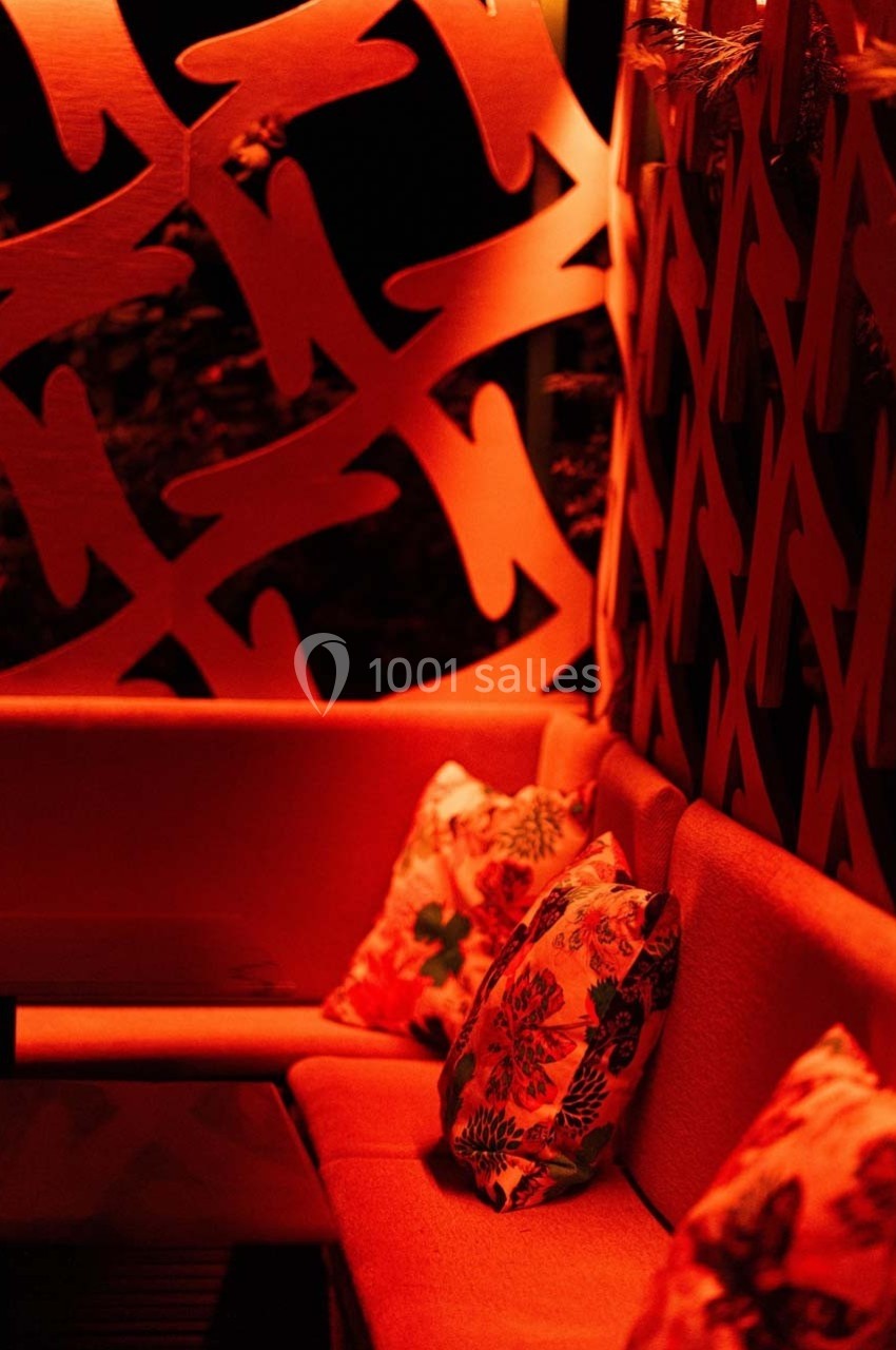 Banquette rouge avec coussins à motifs floraux, entourée de panneaux décoratifs éclairés par une lumière rouge.