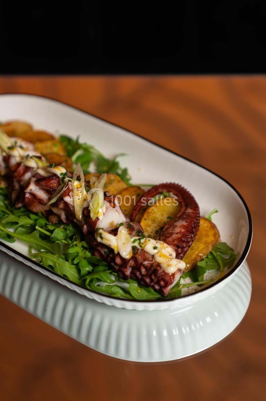 Plat de tentacules de poulpe grillés servis sur un lit de roquette avec des pommes de terre et une garniture.