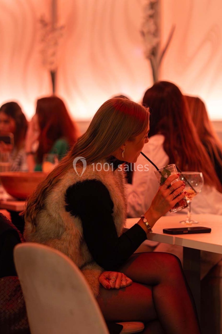 Une femme assise dans un restaurant, buvant une boisson avec une paille, entourée d'autres clients.