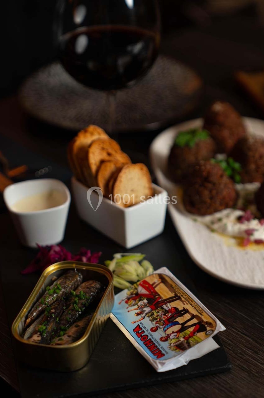 Assiette composée de sardines en boîte, crackers, boulettes de viande et verre de vin rouge sur une table sombre.