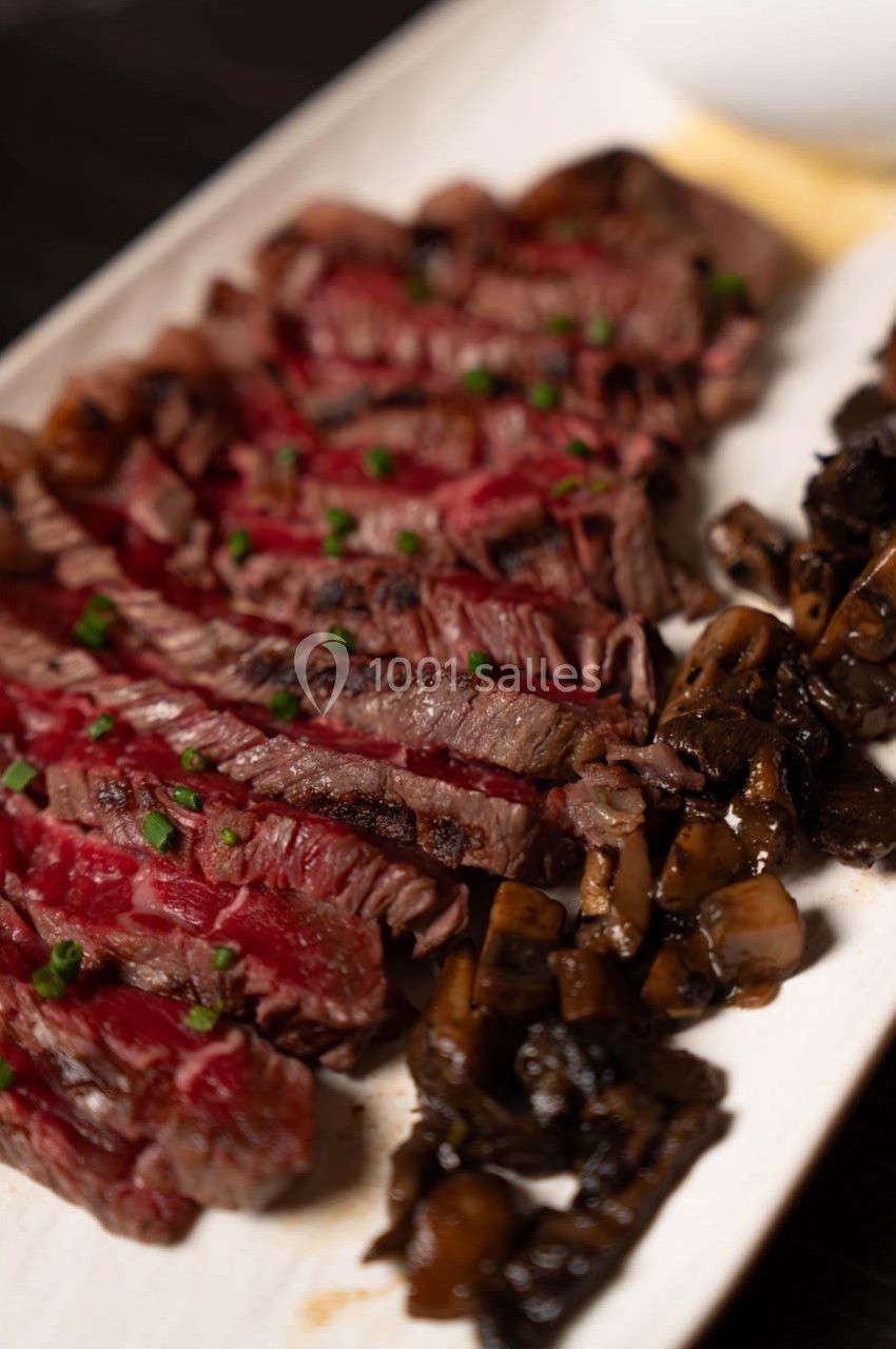 Tranches de viande grillée servies avec des champignons sautés sur une assiette blanche.