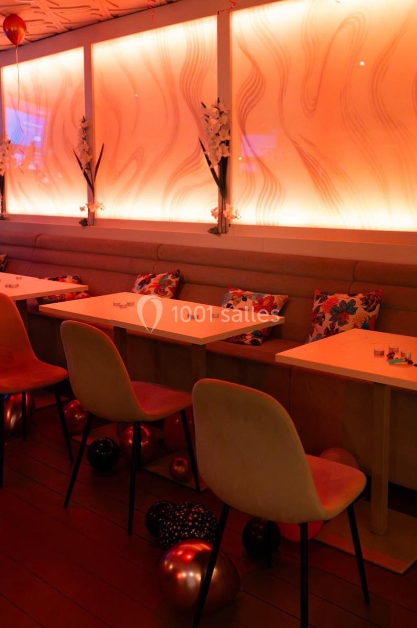 Salle décorée avec des tables alignées, chaises modernes, éclairage orange et ballons au sol.