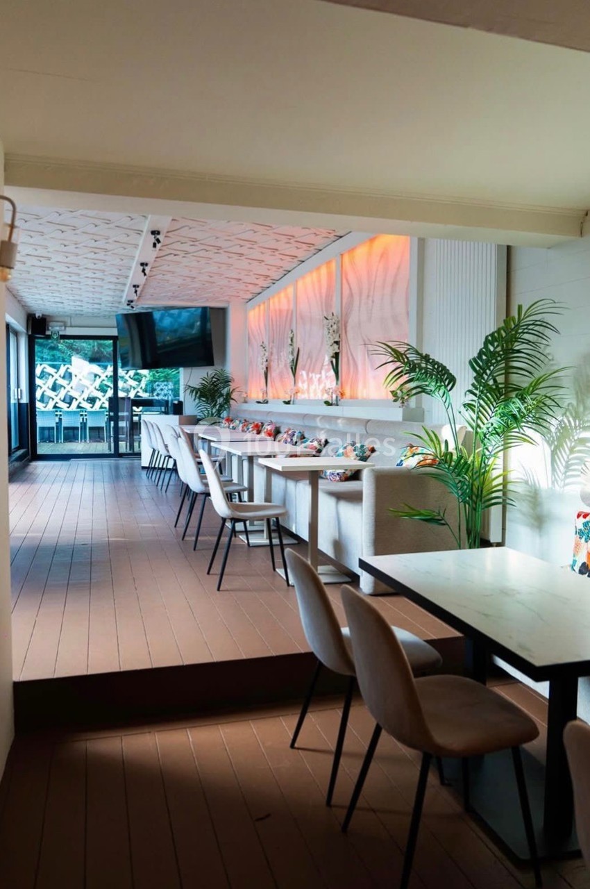 Salle lumineuse avec tables en marbre, chaises rembourrées, plantes décoratives et éclairage mural chaleureux.