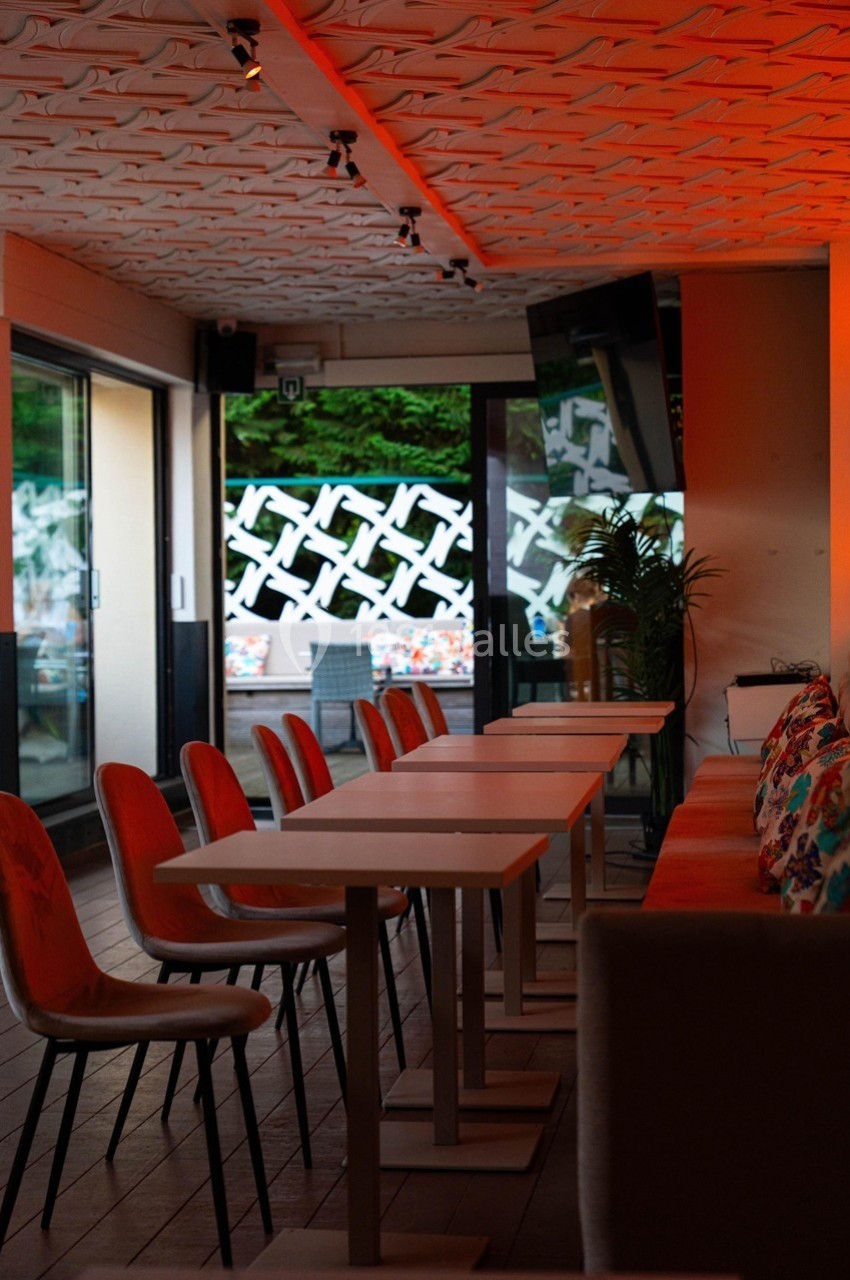 Salle de restaurant moderne avec tables alignées, chaises design et lumière tamisée, donnant sur une terrasse extérieure.