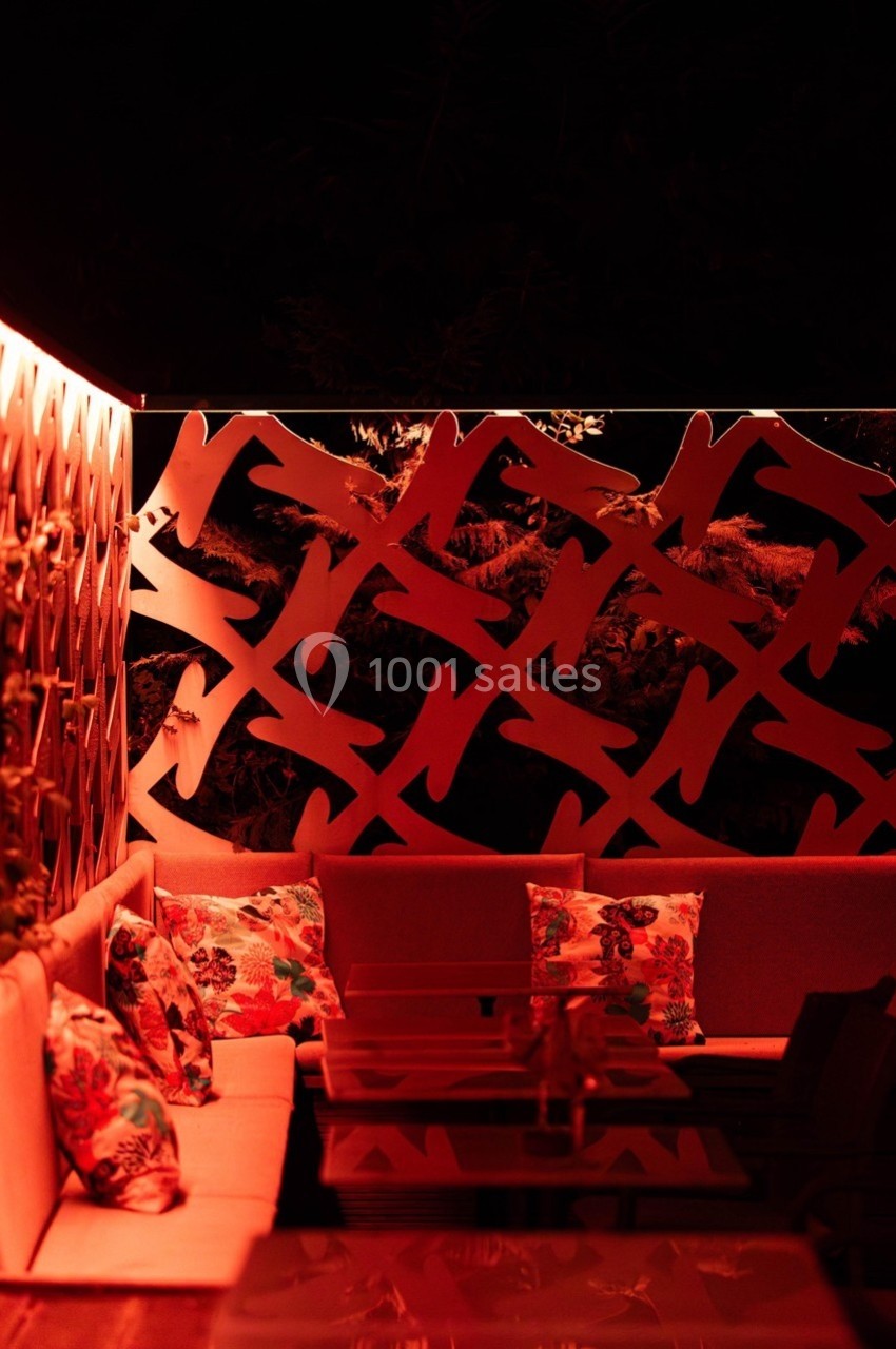 Espace extérieur avec banquettes, coussins colorés et éclairage rouge tamisé, décoré d'un panneau ajouré.