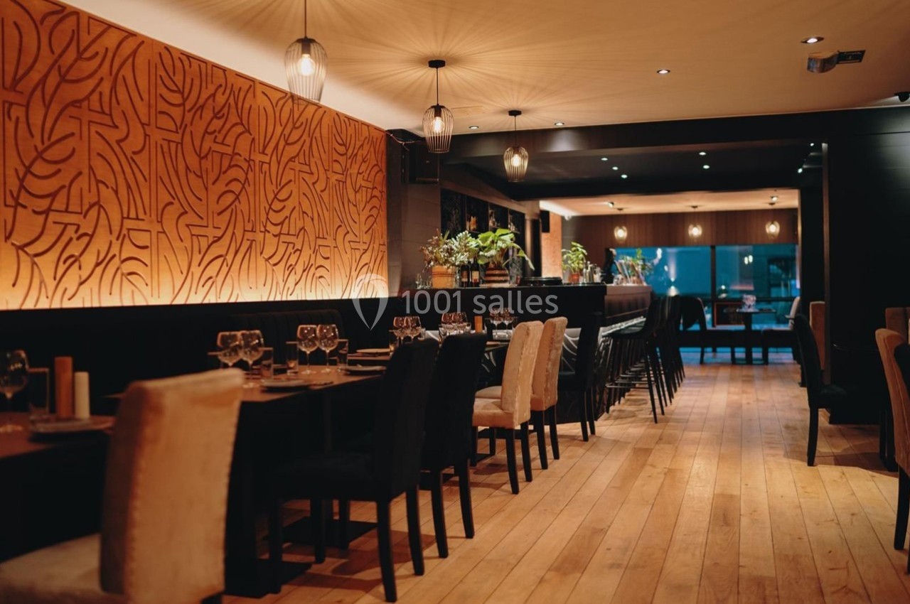 Salle de restaurant élégante avec tables dressées, éclairage tamisé et mur décoré de motifs végétaux.