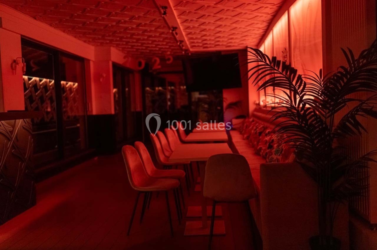 Salle de restaurant vide éclairée par une lumière rouge tamisée, avec des chaises alignées le long d'une table.