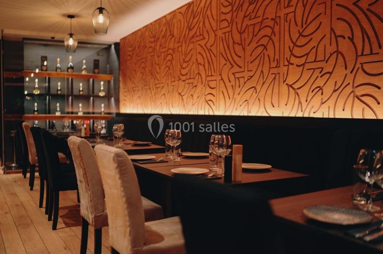 Salle de restaurant élégante avec tables dressées, chaises rembourrées et mur décoré de motifs abstraits éclairés.