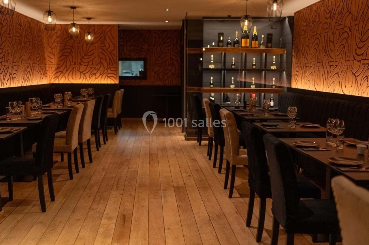 Salle de restaurant élégante avec tables dressées, éclairage tamisé et étagères de bouteilles en arrière-plan.