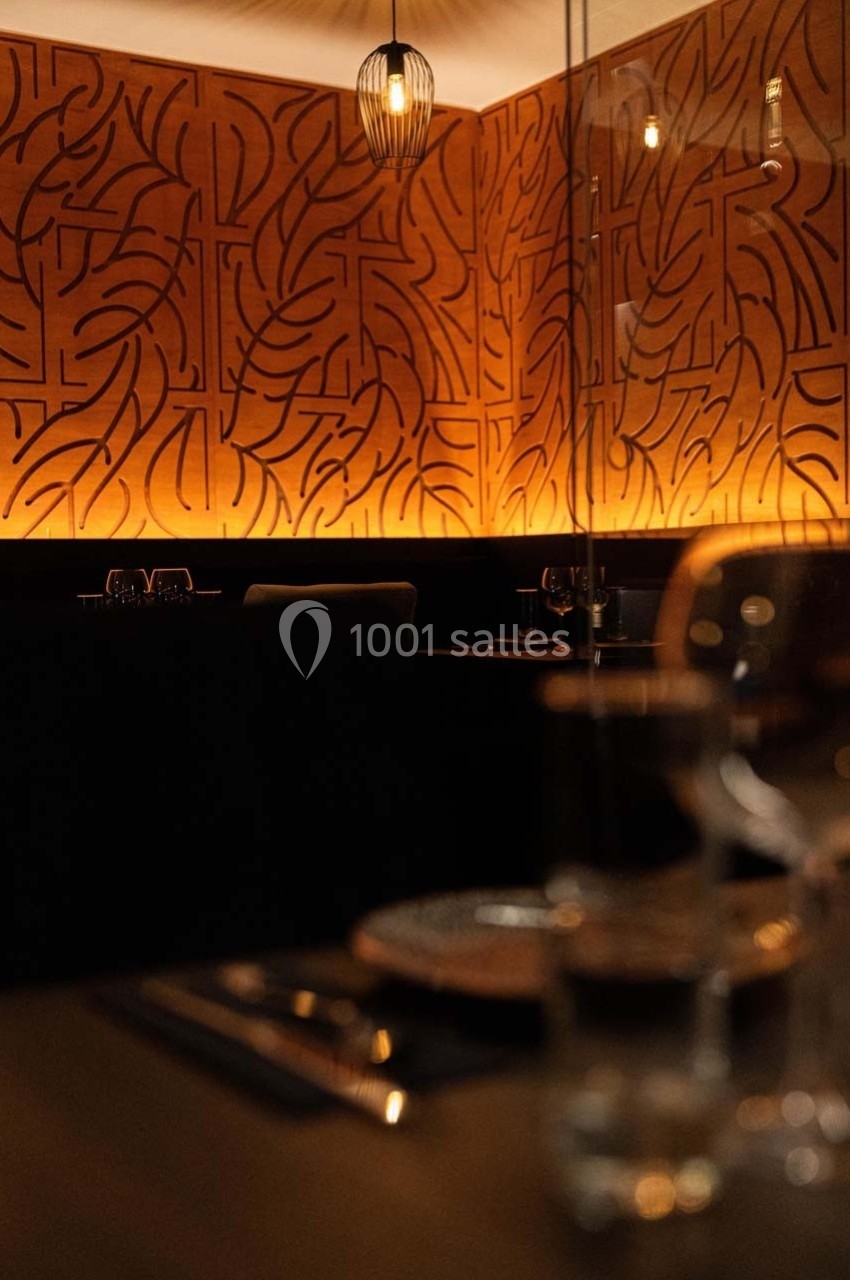 Salle de restaurant avec éclairage tamisé, décor mural géométrique et table dressée au premier plan.