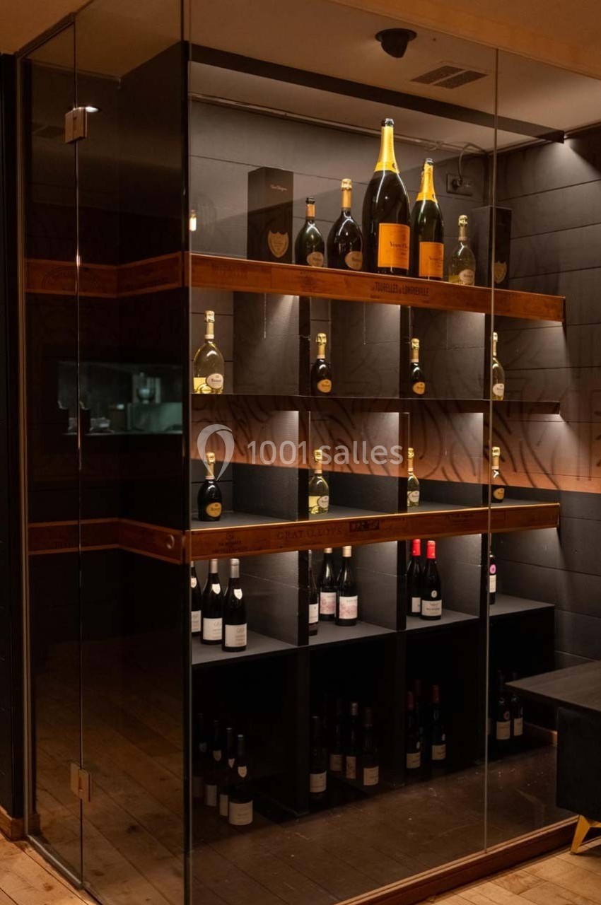 Cave vitrée avec étagères en bois, contenant des bouteilles de vin et de champagne exposées sous un éclairage tamisé.