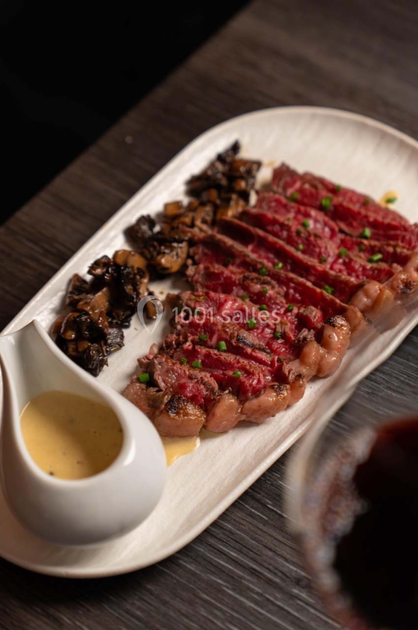 Tranches de viande rouge saignante avec champignons sautés et sauce servie dans une saucière blanche.