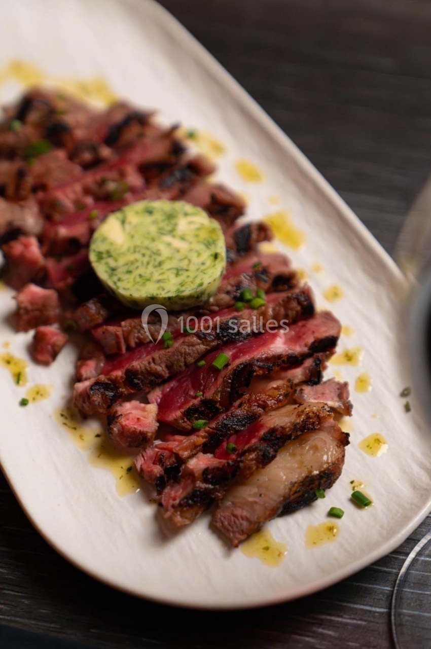 Tranches de steak grillé garnies de beurre aux herbes, servies sur une assiette blanche avec une sauce légère.