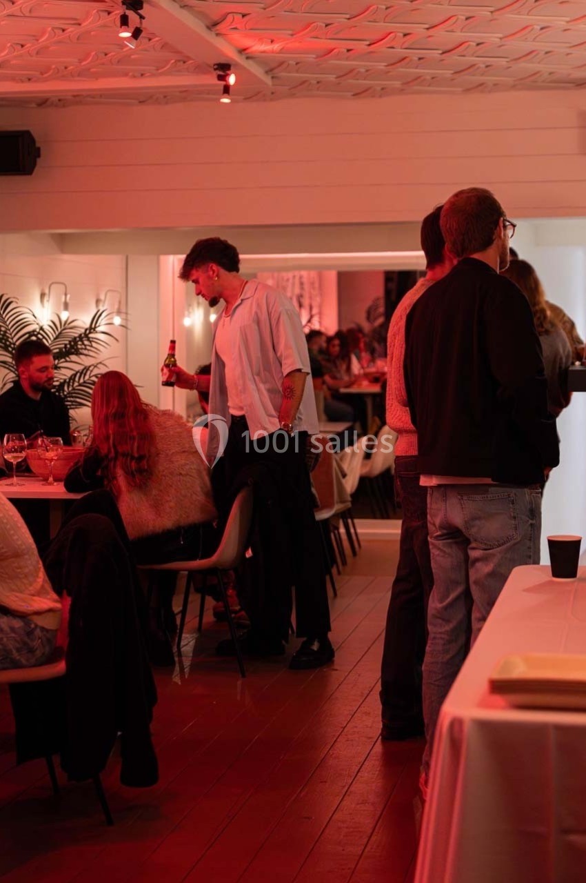 Des personnes discutent et partagent un moment convivial dans un espace intérieur éclairé par une lumière rouge tamisée.