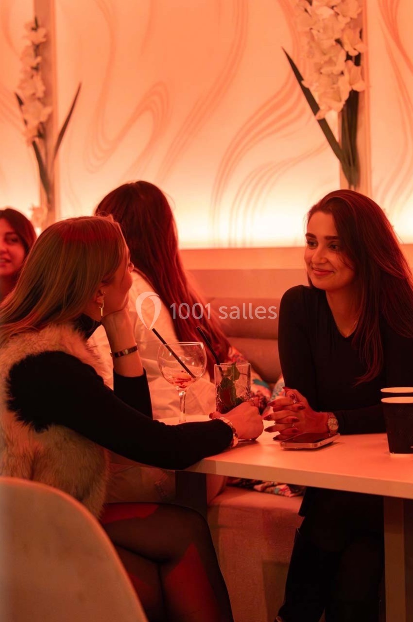 Deux femmes discutent à une table dans un café à l'éclairage chaleureux, entourées d'autres clients.