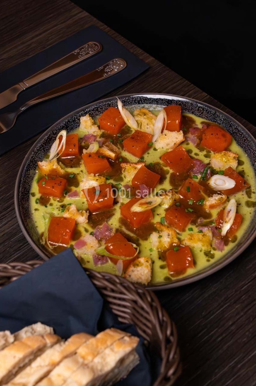 Assiette de cubes de potiron, oignons nouveaux, croûtons et sauce, servie sur une table avec du pain en panier.