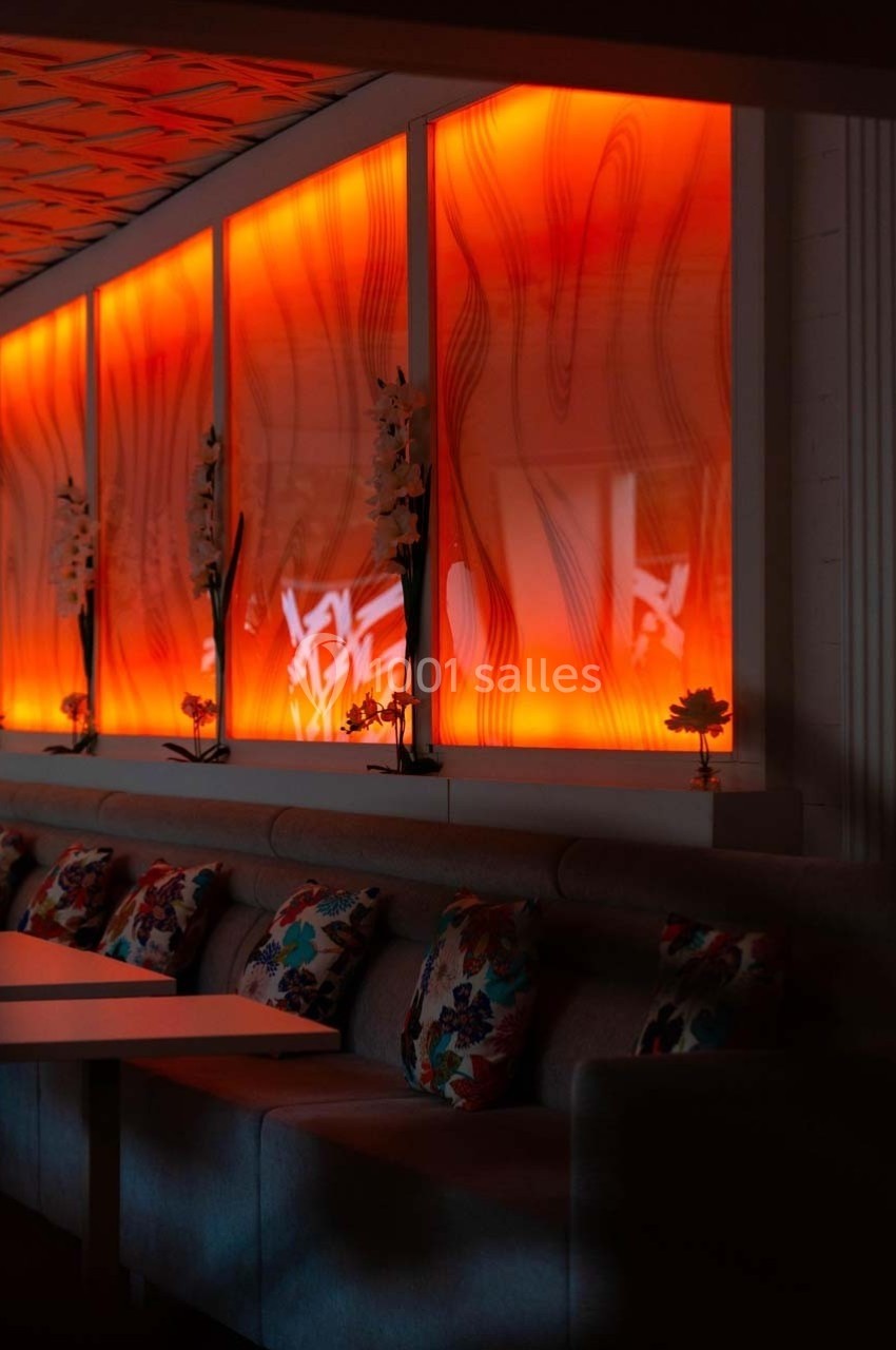 Mur rétroéclairé orange avec motifs abstraits, banquette grise et coussins colorés dans un espace intérieur moderne.