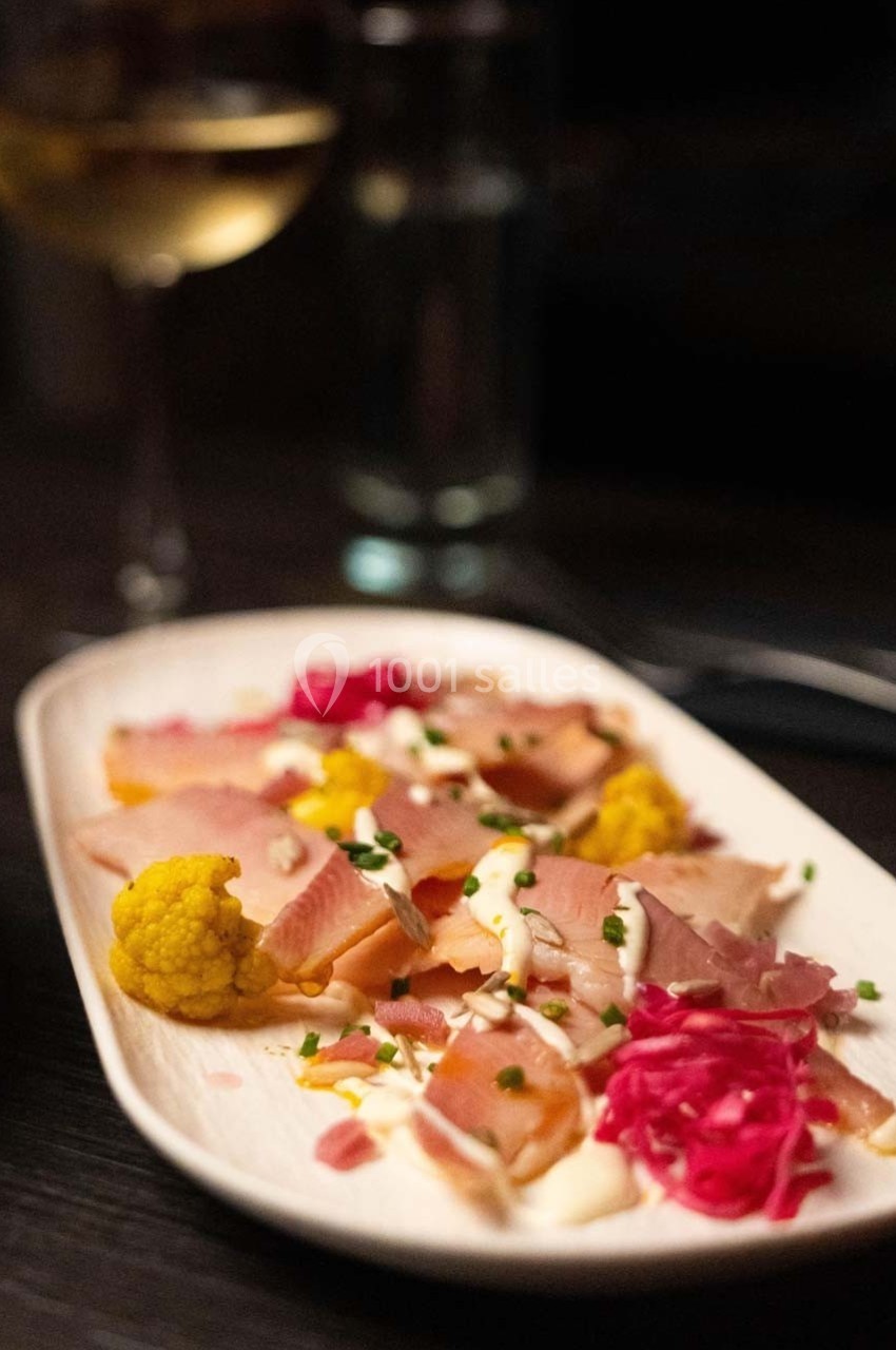 Assiette de charcuterie avec jambon, chou-fleur jaune, choux rouges et ciboulette, servie sur une table sombre.