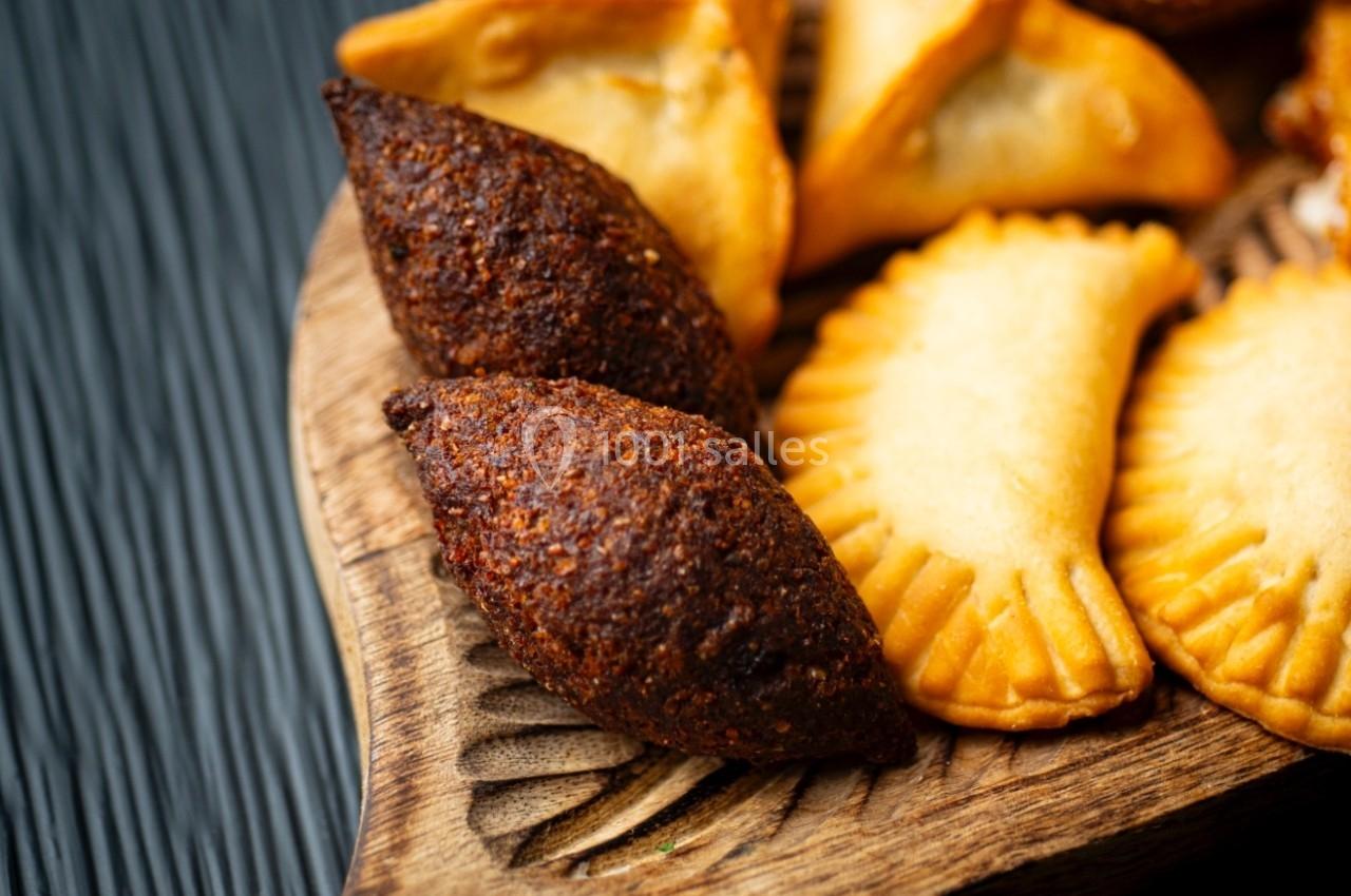 Assortiment de beignets et de pâtisseries salées disposés sur un plateau en bois, posé sur une surface sombre.