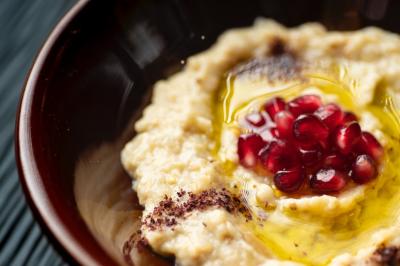 Purée de pois chiches garnie de graines de grenade, huile d'olive et épices, servie dans un bol brun.