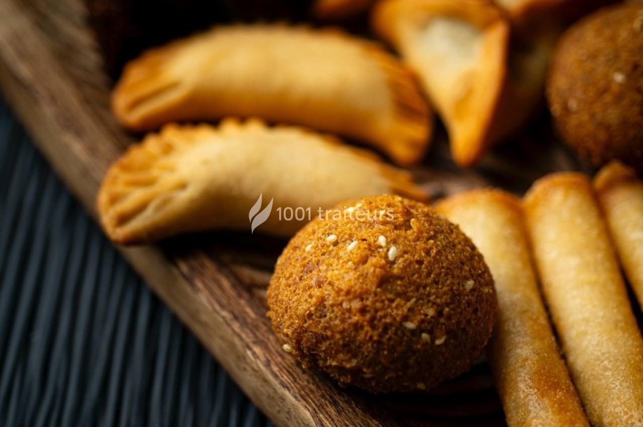 Assortiment de snacks salés comprenant des samoussas, des falafels et des rouleaux croustillants sur un plateau en bois.