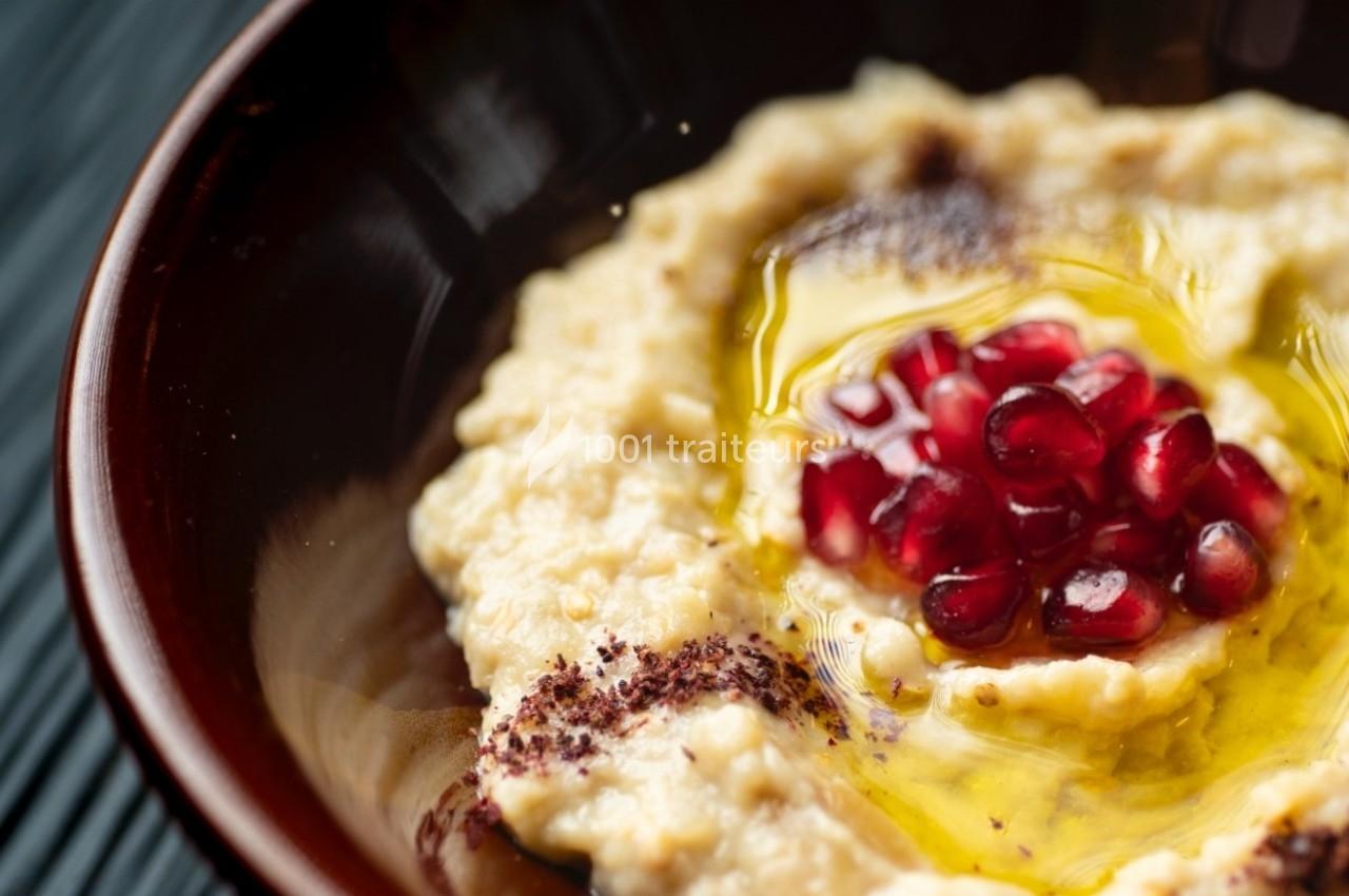 Purée de pois chiches garnie de graines de grenade, huile d'olive et épices, servie dans un bol brun.