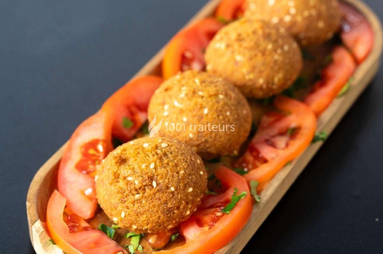 Assiette en bois contenant des falafels dorés entourés de tranches de tomates fraîches et de persil haché.