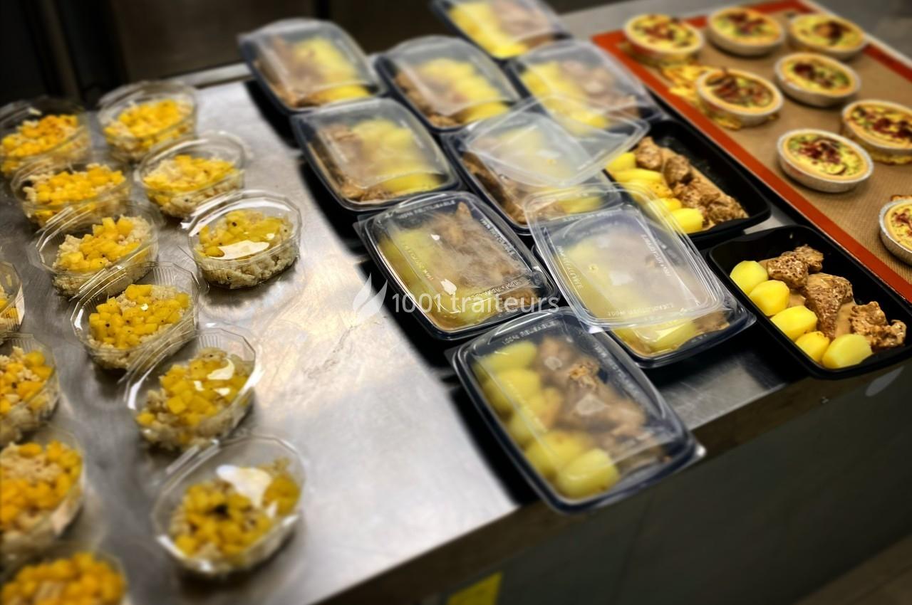 Repas préparés disposés sur un plan de travail, comprenant salades, plats principaux et desserts emballés.