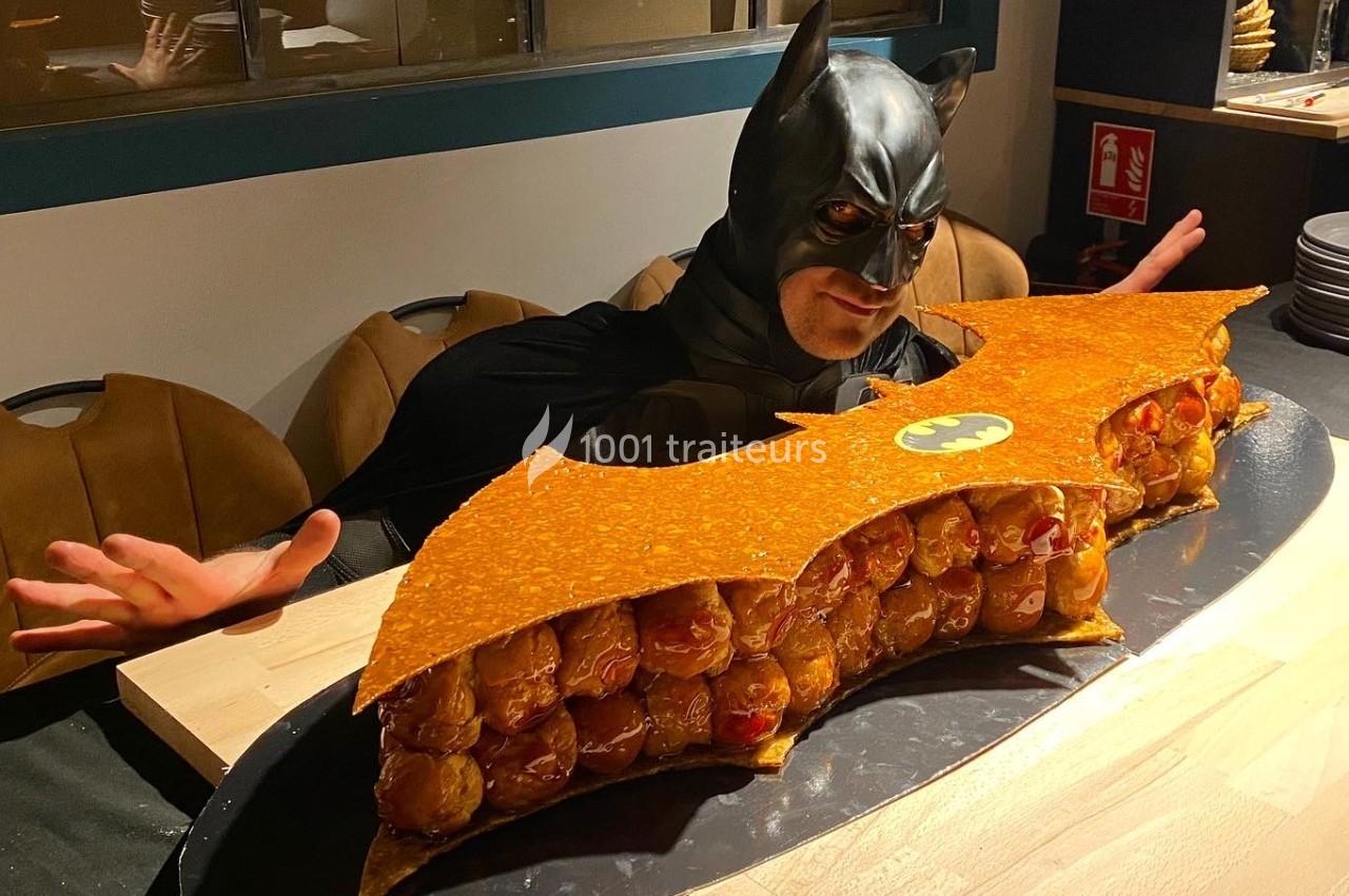Un homme déguisé en Batman pose derrière une pièce montée en forme de logo de chauve-souris.