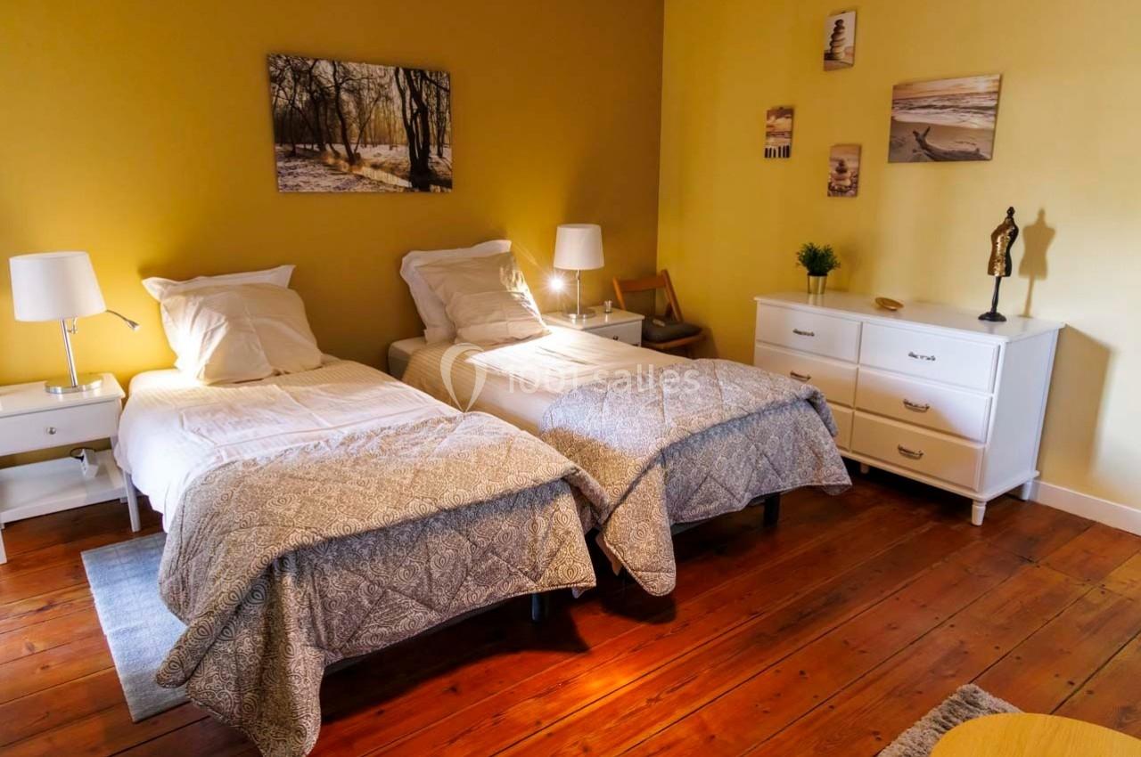 Chambre avec deux lits simples, parquet en bois, murs jaunes, mobilier blanc et décorations murales.