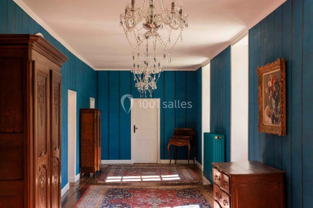 Intérieur d'une pièce avec murs bleus, meubles en bois, lustres en cristal et tapis colorés au sol.