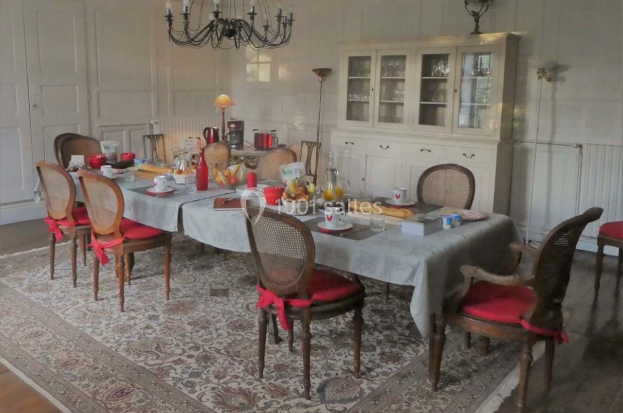 Table dressée pour le petit-déjeuner dans une salle à manger élégante avec chaises en bois et buffet en arrière-plan.