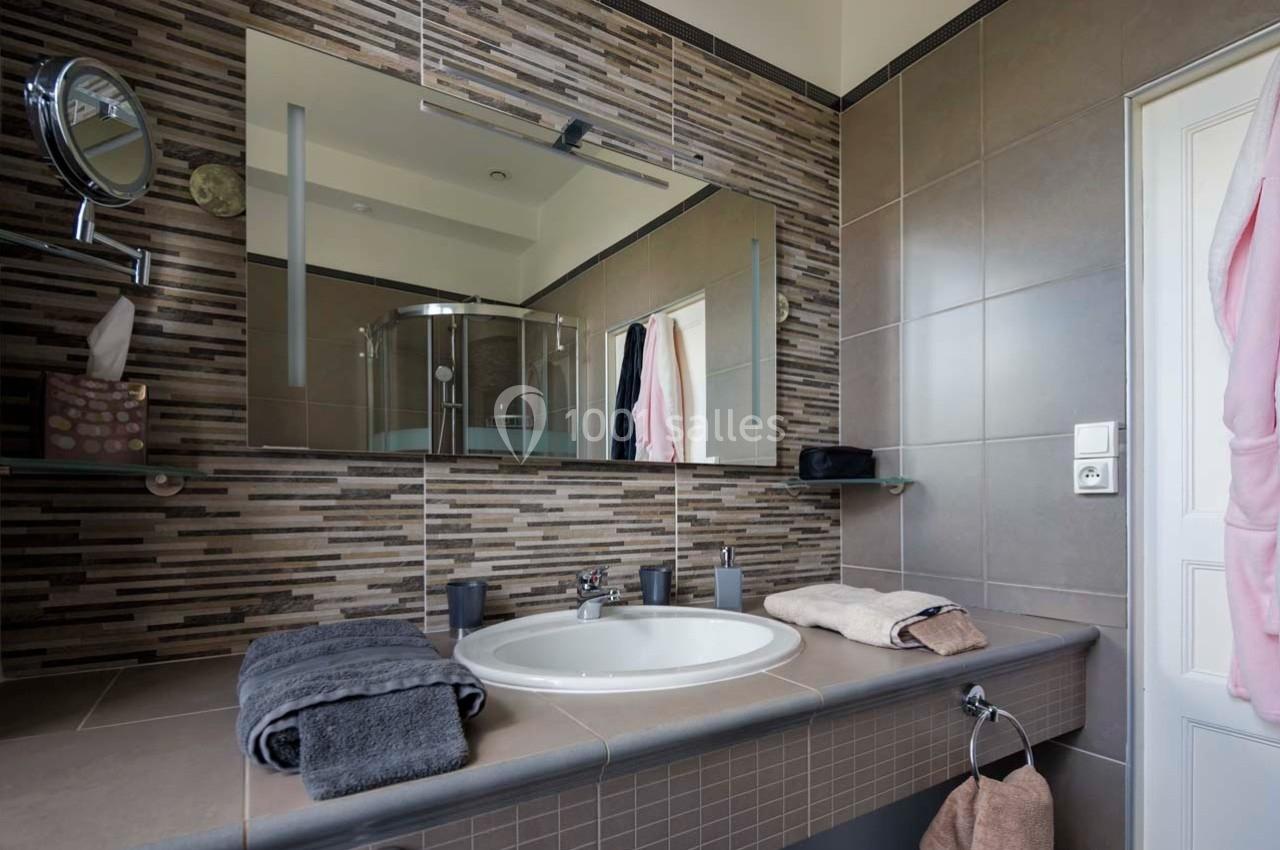 Salle de bain moderne avec lavabo, miroir, douche vitrée et serviettes pliées sur le plan de travail.