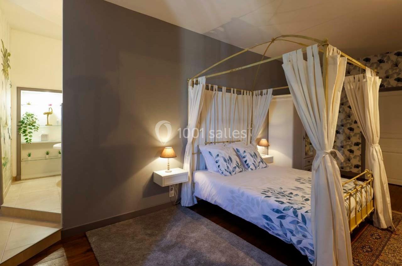 Lit à baldaquin avec draperies blanches dans une chambre lumineuse, attenante à une salle de bain moderne.