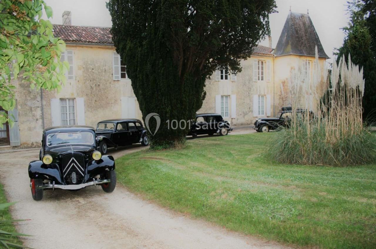 Voitures anciennes garées devant un manoir en pierre entouré de pelouse et d'arbres.