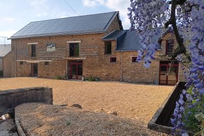 Cour extérieure ensoleillée avec des tentes noires, des fleurs en pot et une maison en pierre en arrière-plan.