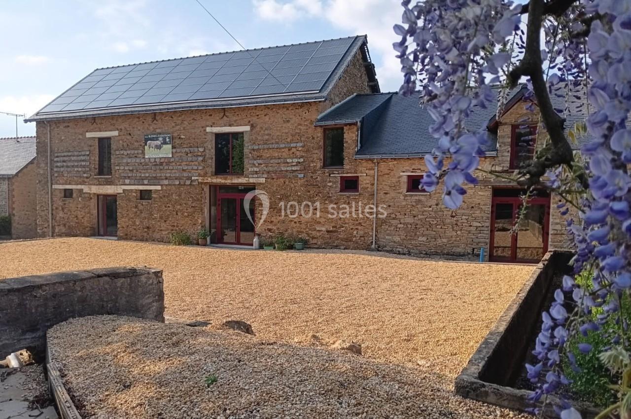 Façade en pierre d'une maison rénovée avec panneaux solaires sur le toit, entourée d'une cour en gravier et de glycines en…