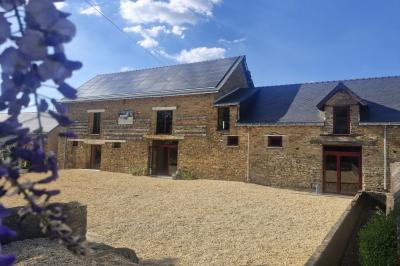 Cour extérieure ensoleillée avec des tentes noires, des fleurs en pot et une maison en pierre en arrière-plan.