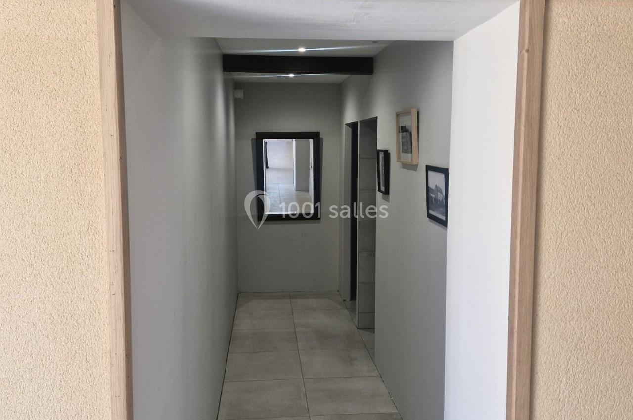 Vue d'un couloir étroit avec un panneau ’Toilettes’ en bois au-dessus de l'entrée, murs clairs et sol carrelé.