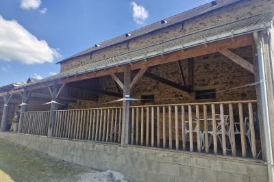 Cour extérieure ensoleillée avec des tentes noires, des fleurs en pot et une maison en pierre en arrière-plan.