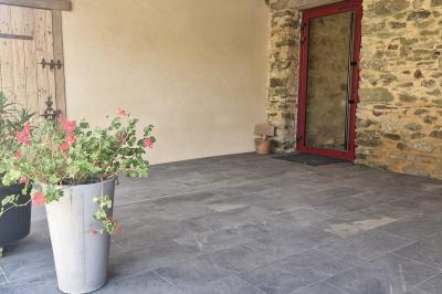 Cour extérieure ensoleillée avec des tentes noires, des fleurs en pot et une maison en pierre en arrière-plan.