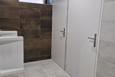 Cour extérieure ensoleillée avec des tentes noires, des fleurs en pot et une maison en pierre en arrière-plan.