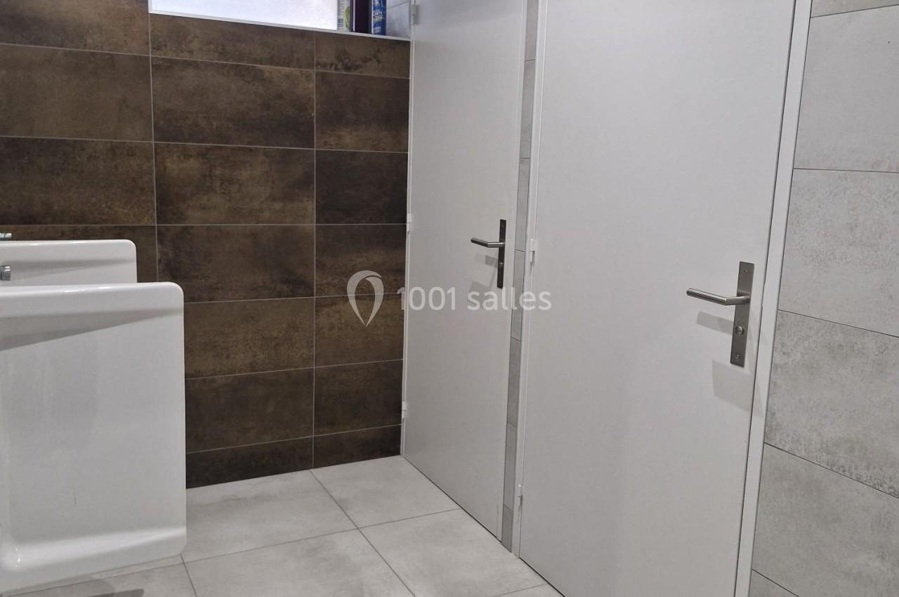 Deux portes blanches dans une pièce avec carrelage beige et marron, un lavabo et une étagère en hauteur.